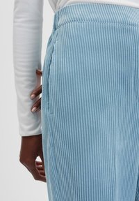 Pantalon en velours côtelé bleu clair avec des rayures verticales, présentant une taille ajustée et des poches latérales pour une silhouette structurée.