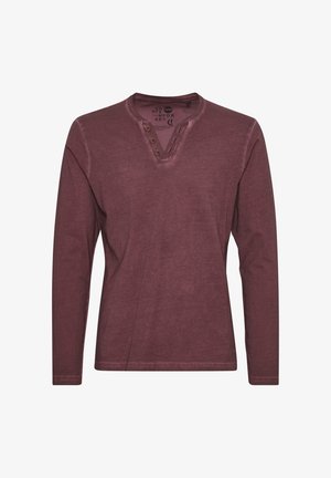 Burgundska srajca dolgimi rokavi iz mehkega materiala, z henley ovratnikom in tremi gumbi ter vidnimi šivi.