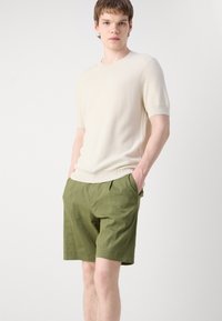 Maglione corto a maniche corte color beige chiaro a costine abbinato a pantaloni corti verdi larghi. I pantaloni corti presentano tasche laterali e una vestibilità comoda.