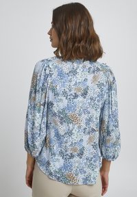 Kvetovaná blúzka s nariasenými rukávmi, s modrým, zeleným a hnedým vzorom na svetlom pozadí; mäkká tkanina s uvoľneným strihom.