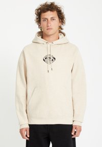 Beige hoodie gemaakt van zachte stof, met een centraal zwart logo ontwerp, koordjes en een voorzak in kangoeroestijl. De mouwboorden zijn geribbeld.