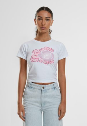 White, cropped t-shirt featuring pink graphic text that reads "Can I give you a kiss," with cartoon lips and a bubble. Short sleeves, round neckline.