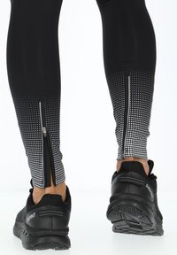 Zwarte sportleggings met een grijsgradatie patroon met stippen aan de onderkant, voorzien van ritsen bij de enkels en gecombineerd met zwarte sneakers.