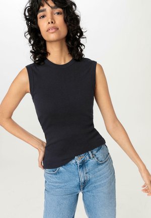 Black sleeveless top in cotton blend with a fitted silhouette, round neckline, and smooth texture, paired with light blue high-waisted jeans.