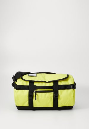 Saco de desporto amarelo com detalhes em preto, feito de material durável. Apresenta um fecho de aba, faixa de ombro ajustável e um bolso frontal com zipper.