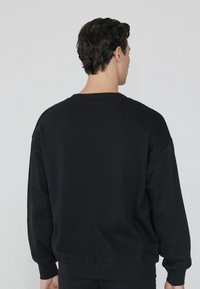 Zwarte sweatshirt, oversized pasvorm, zachte textuur, ronde hals, ribgebreide manchetten en onderkant, minimalistisch ontwerp, gladde stof, geen zichtbare logo's of patronen.