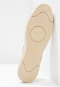 Sohle eines Espadrille-Schuhs, gefertigt aus strukturiertem natürlichem Material in Beige, mit einem runden Logo, das "36" liest, und einem glatten Gummibereich.