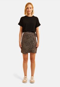 Top de manga corta negro texturizado combinado con una falda envolvente floral marrón y zapatillas ligeras. El conjunto presenta un ajuste relajado y patrones sutiles.
