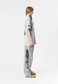Camiseta gris de gran tamaño con un corte en la espalda y un diseño impreso, combinada con pantalones grises que presentan gráficos laterales y detalles de cordón.