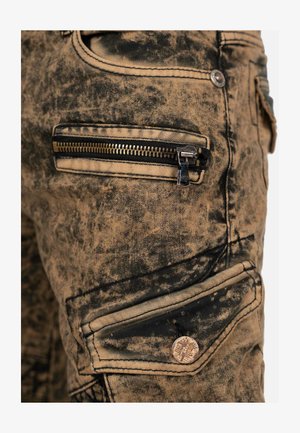 Jeans-Cargohose in verblasstem Beige mit schwarzem Sprenkelmuster, ausgestattet mit flachen Fronttaschen, Reißverschlüssen und Messingbeschlägen.