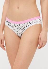 Lenjerie albă cu puncte negre, având un braț elastic roz. Oferă un design simplu și o textură netedă. Potrivită pentru purtarea zilnică.