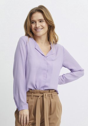 Light purple long-sleeve blouse with a V-shaped collar and button closure, paired with high-waisted tan trousers featuring a fabric belt.