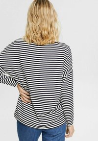 Maglia a maniche lunghe a righe in blu navy e bianco. Presenta una vestibilità comoda, maniche ampie e un orlo curvo. Il tessuto sembra morbido e leggero.