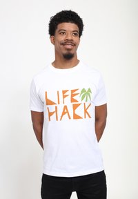 Bílá tričko s krátkým rukávem, na kterém se nachází výrazný oranžový text "LIFE HACK" a grafika zelené palmy, vyrobené z bavlněné látky.