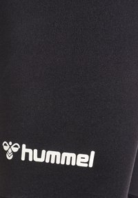 Svarta sportshorts i elastiskt material, med en framträdande vit "hummel"-logotyp och en jämn, slät yta.