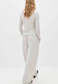 Graues, langärmliges Oberteil, kombiniert mit weit geschnittenen Jogginghosen, beide aus weichem Material. Besitzt einen lässigen Schnitt und ein schlichtes Design ohne sichtbare Muster.