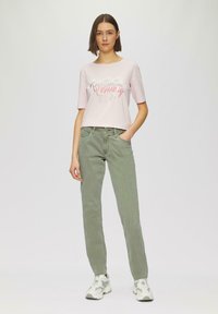 Helles rosa, kurzes T-Shirt mit dem Text "Positive Positivity", kombiniert mit grünen geraden Jeans und weißen Turnschuhen. Einfaches, lässiges Outfit.
