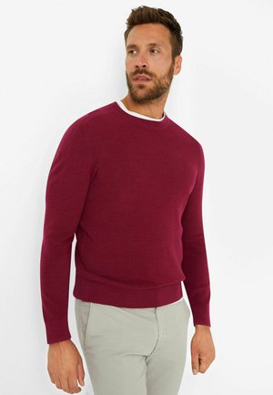 Maroon knitted sweater with a ribbed texture, crew neckline, and long sleeves. The hem and cuffs are fitted, complementing light-colored pants.