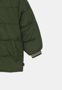Chaqueta acolchada verde con diseño de acolchado, bolsillo frontal y puños acanalados con rayas en contraste. Textura de tela suave.