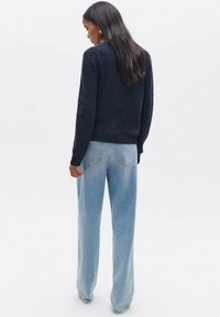 Maglione navy a trama con scollatura ampia e polsini a costine, abbinato a jeans dritti azzurri chiari con delicate cuciture sulle tasche posteriori.