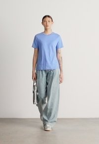 Svetlo modra bombažna majica s kratkimi rokavi, kombinirana z ohlapnimi svetlimi kavbojkami in srebrnimi supergami, držala kovinsko torbico.