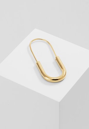 Goldfarbener Metall-Sicherheitsnadel-Design mit einer glatten, runden Form und einer polierten Oberfläche, die auf einer weißen geometrischen Plattform ruht.