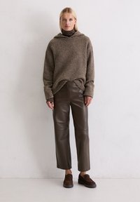 Brązowy, dzianinowy hoodie z kapturem, w połączeniu z brązowymi, skórzanymi spodniami taper oraz ciemnobrązowymi butami na slip-on. Różnorodne tekstury i warstwowy krój.
