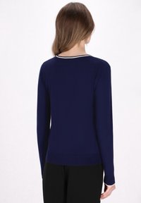 Tummansiniharmaa neulepaita pitkillä hihoilla, ribbetyt hihansuut ja helma sekä kontrastivärinen kaulus. Pehmeä rakenne ja slim fit -design.