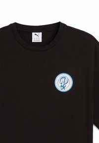 Sort bomulds T-shirt med rund halsudskæring og et cirkulært logo i blå og hvid på venstre brystområde. Glat tekstur.