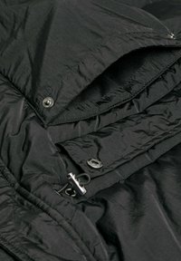 Czarna kurtka puchowa z eleganckim, pikowanym wzorem, zapięciem na napy oraz gładką, lekko odbijającą światło powierzchnią.