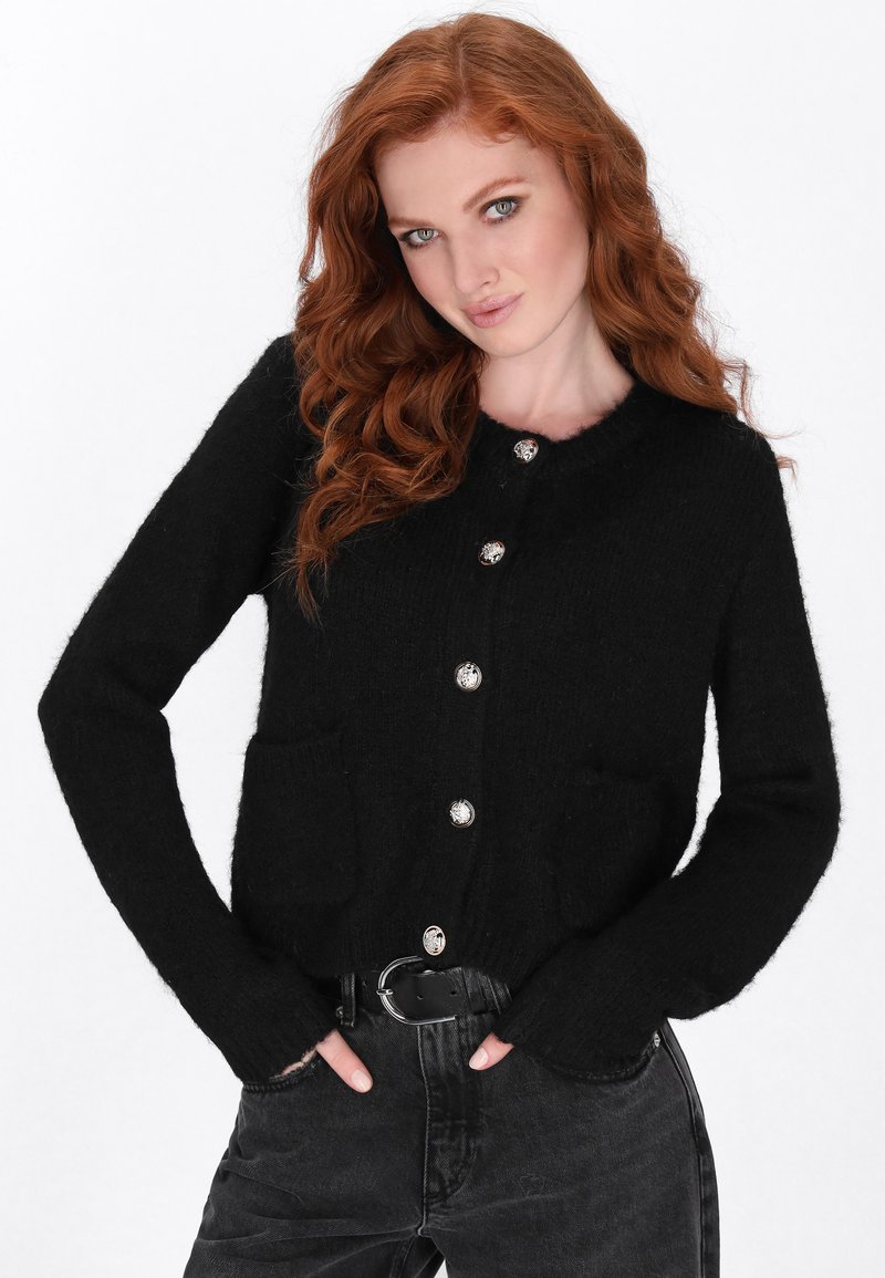 Zwarte cardigan gemaakt van zachte stof, met een ronde hals, lange mouwen, twee voorzakken en zilveren knoopsluitingen.