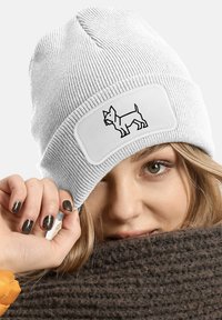 White knitted beanie with a textured finish. Features a patch with a black outline of a dog. Warm and flexible fabric design.