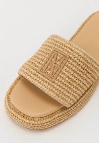 Beige tkané šlapky vyrobené z texturovaného materiálu, s širokým páskem s vyraženým logem a hladkým, světlým hnědým stélkou.