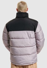 Padded bunda s čiernou hornou časťou a svetlofialovou dolnou časťou, s vysokým golierom a prešívanou textúrou, vhodná do chladného počasia.