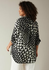 Blusa de patrón de espiga en blanco y negro con un corte relajado, mangas enrolladas y un dobladillo redondeado. Fabricada con una tela ligera y texturizada.