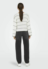 Lekki, luźno dziany kremowy sweter z szarymi paskami. Połączony z czarnymi dżinsami z wysokim stanem i białymi trampkami.