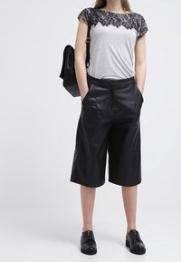 Šedé tričko s černými krajkovými detaily na ramenech, doplněné černými koženými kalhotami culottes a černými nazouvacími botami. Černá kabelka na rameni.