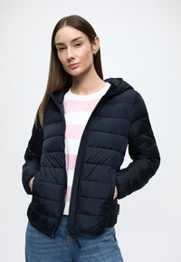 Μπλε-σκούρο μπουφάν τύπου puffer με υφή, που διαθέτει κουκούλα, κλείσιμο με φερμουάρ και πλαϊνές τσέπες, συνδυασμένο με ριγέ λευκό και ροζ πουκάμισο.