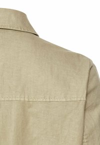 Beige linned skjorte med en krave på ryggen, der har en glat tekstur og syninger langs skuldersømmen.