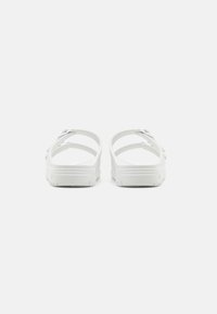 Sandali bianchi con superficie liscia, cinturini regolabili e suola imbottita. Presentano un design semplice con minime decorazioni hardware.