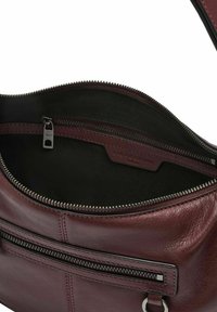 Wnętrze torby z bordowej skóry z zamykanym na zamek kieszonką i czarną podszewką. Wyposażona w srebrny zamek i metkę z logo na skórze.