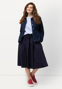 Denimjack, gestreept shirt, marineblauwe midirok met een strik aan de voorkant, en rode instapper-schoenen met witte zolen. Casual, gelaagde outfit.