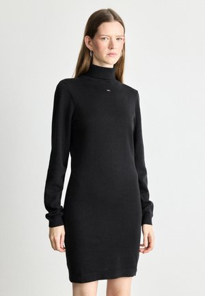 Vestido negro de cuello alto hecho de un material suave, silueta ajustada, mangas largas y un pequeño logotipo en el pecho.