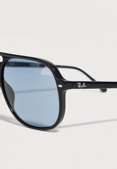 Черни слънчеви очила Ray-Ban с правоъгълни сини стъкла и тънки рамки на бял фон.