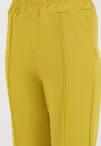 Gele stofbroek met een gladde textuur, voorzien van een elastische tailleband en zijnaad voor een slim fit en comfort.