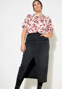 Witte kortemouwen shirt met kleurrijke bloemen- en drakenafdruk; gecombineerd met een middellange zwarte denimrok met een split aan de voorkant en een franjeonderkant.