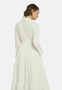Weißes Langarmkleid mit tailliertem Oberteil und gestuftem Rock. Verfügt über eine taillierte Taille und dezenten Stofftextur.