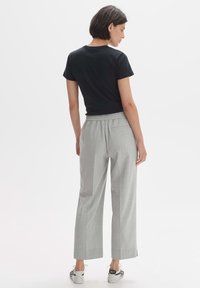 Black short-sleeve fitted t-shirt paired with light gray wide-leg pants, featuring an elastic waistband and side slits, with casual shoes.
