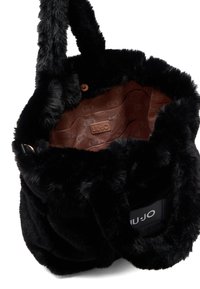 Borsa a tracolla in finta pelliccia nera con una texture morbida, corpo soffice e un interno marrone con motivo che presenta un'etichetta con logo. Include manici corti avvolti.