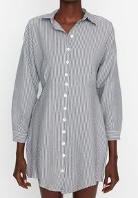 Chemise à rayures noir et blanc, dotée de manches longues, d'un col et d'une poche poitrine. Tissu lisse avec une coupe décontractée.